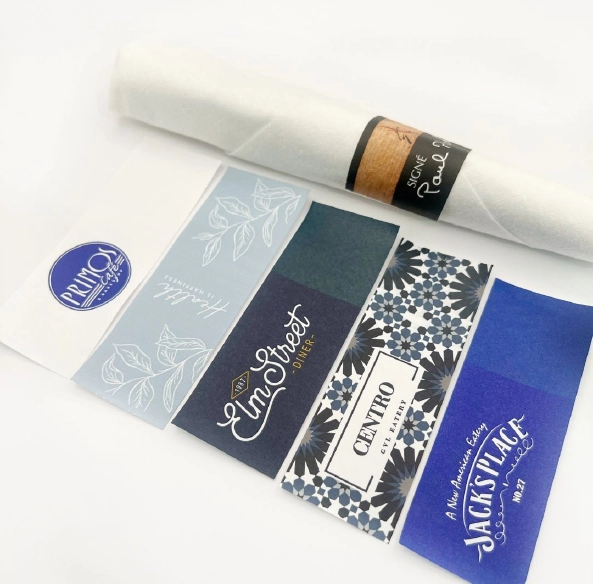 custom-printed-restaurant-napkin-bands-and-wraps Assortment of custom-printed restaurant napkin bands and silverware wraps featuring branded designs for restaurants, hotels, catering companies, and hospitality venues.